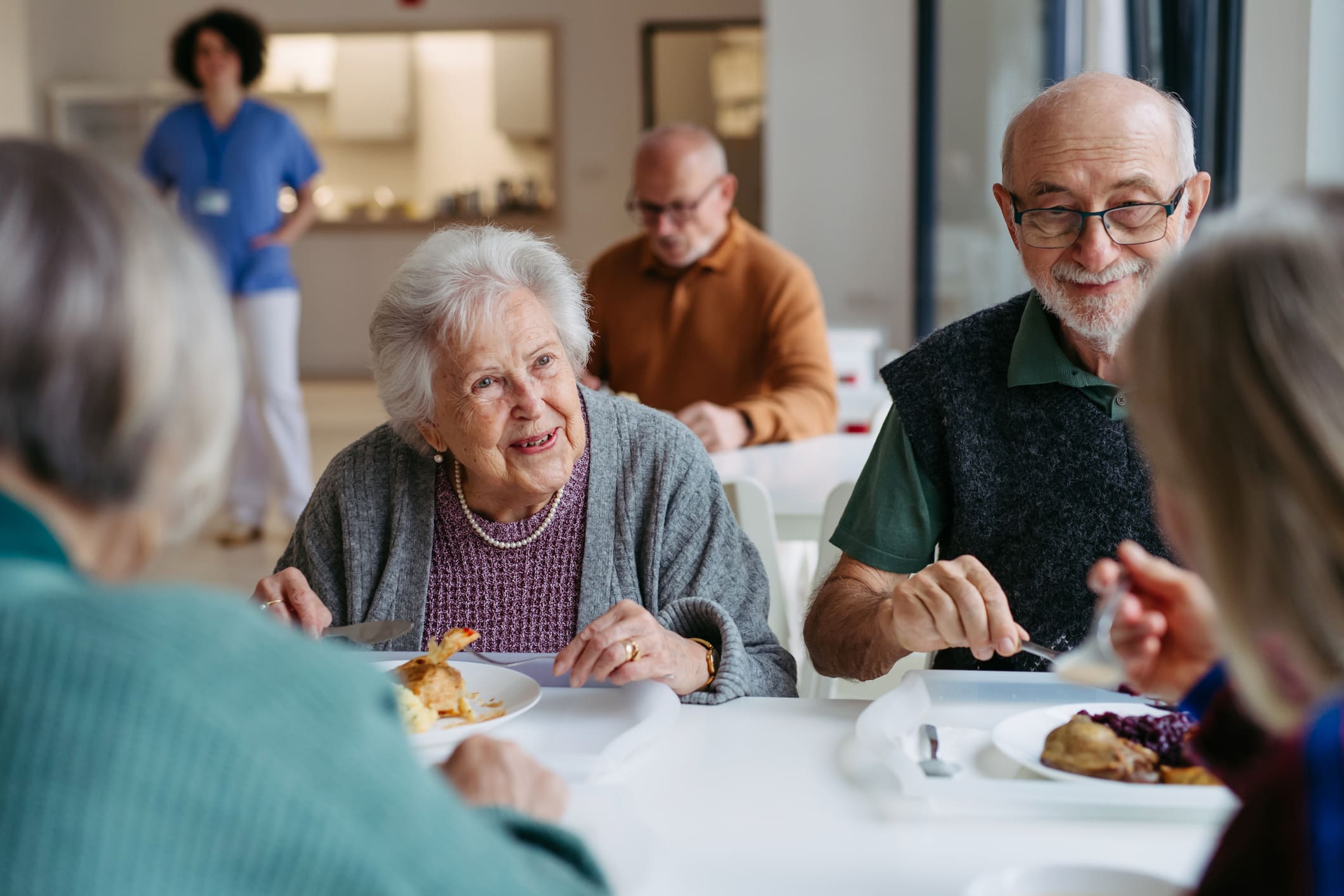 Äldre man och kvinna äter lunch vid ett bord, med andra personer i bakgrunden.