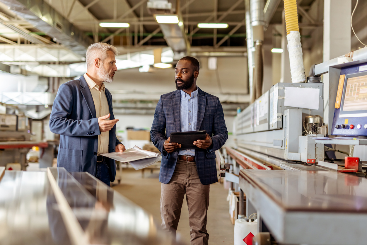 Two Professionals Discussing Processes on Manufacturing Floor with Digital Interface