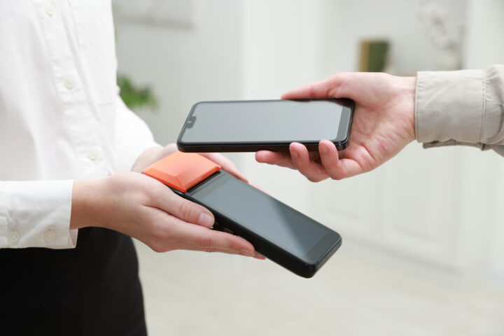 Woman paying for service with smartphone via terminal indoors, closeup